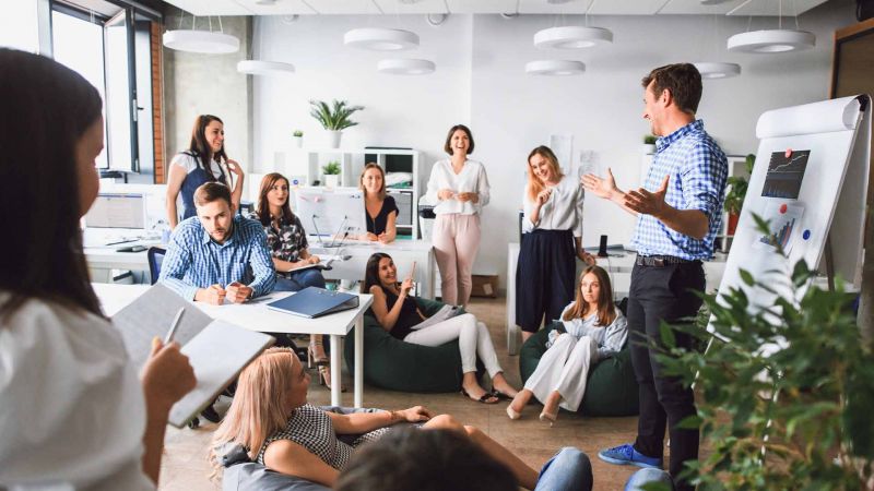 Teammeeting im modernen BÃ¼ro mit Mitarbeiter, der eine PrÃ¤sentation hÃ¤lt, zeigt Kommunikations- und FÃ¼hrungsfÃ¤higkeiten.