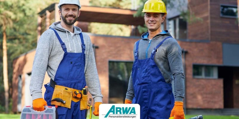 Zwei Handwerker in blauer Arbeitskleidung und Sicherheitshelmen stehen vor einem modernen Gebäude. Beide tragen Werkzeugkisten und sind bereit für den Einsatz. Das Logo von ARWA Personaldienstleistungen ist im Vordergrund zu sehen.