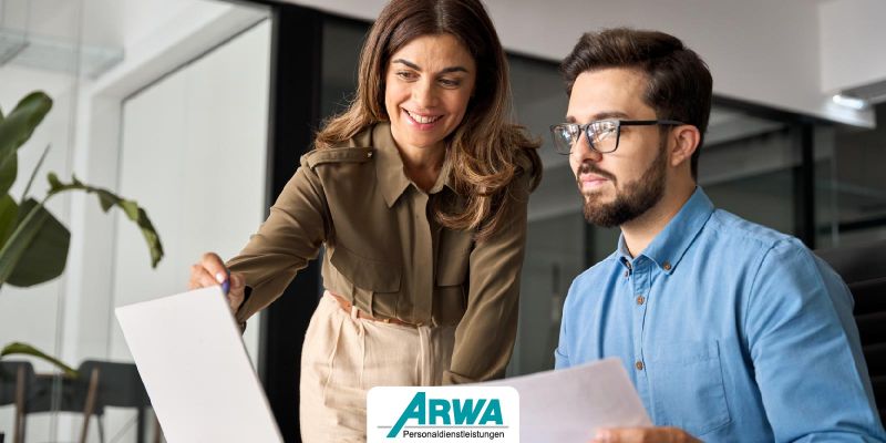 Frau und Mann in einem modernen Büro betrachten ein Dokument, das die Themen Lernbereitschaft und Zusammenarbeit symbolisiert. ARWA Personaldienstleistungen Logo im Vordergrund.