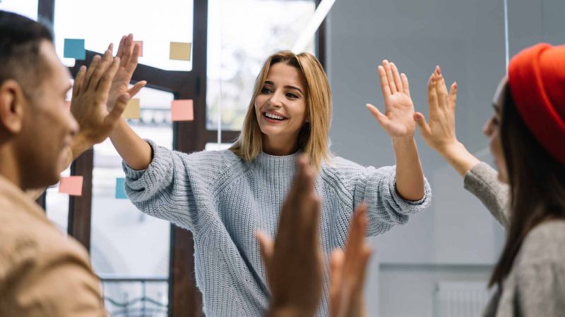 Teamgeist stÃ¤rken: Drei lÃ¤chelnde Kollegen geben sich in einem modernen BÃ¼ro High-Fives