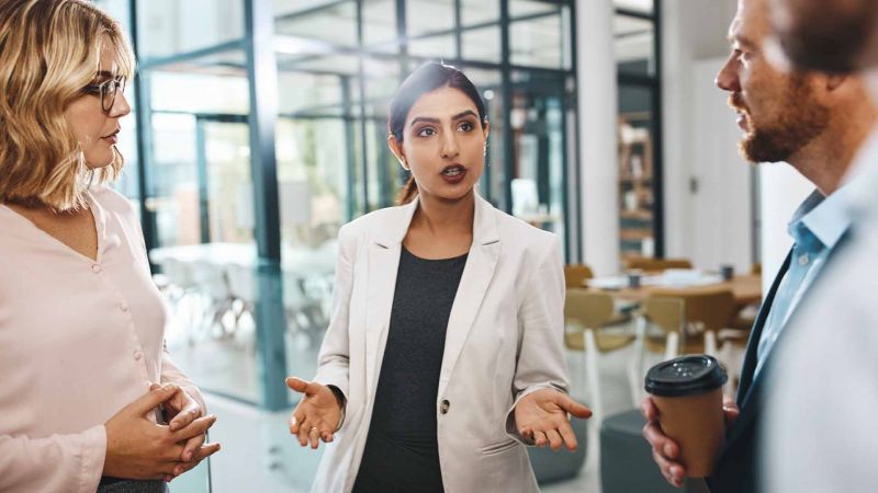 Drei berufstÃ¤tige Personen im intensiven GesprÃ¤ch in einem modernen BÃ¼ro, symbolisiert offene Kommunikation und ProblemlÃ¶sung im beruflichen Kontext.