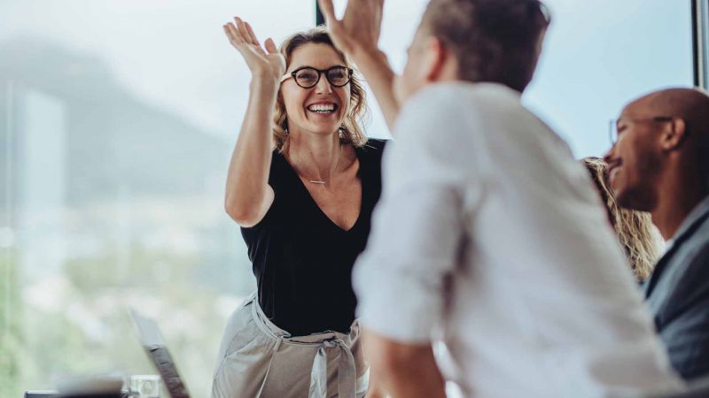 LÃ¤chelnde Frau gibt einem Kollegen ein High-Five in einem Teammeeting. Symbolisiert Teamwork, Zusammenarbeit und positive ArbeitsatmosphÃ¤re.