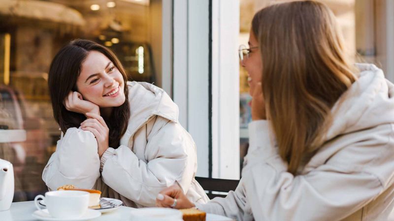 Zwei Frauen unterhalten sich freundlich in einem CafÃ©, symbolisiert die FÃ¤higkeit von Introvertierten, in kleinen Gruppen tiefgrÃ¼ndige GesprÃ¤che zu fÃ¼hren.