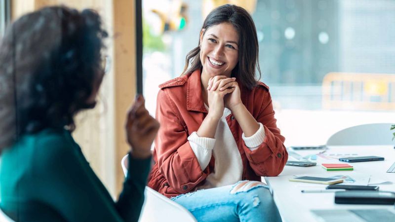 Zwei Frauen fÃ¼hren ein GesprÃ¤ch, wÃ¤hrend eine Frau lÃ¤chelnd und aufmerksam zuhÃ¶rt, was nonverbale Kommunikation durch KÃ¶rpersprache symbolisiert.