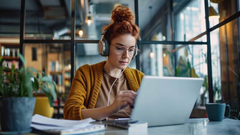 Fokussierte Frau mit KopfhÃ¶rern arbeitet am Laptop in einem ruhigen CafÃ©, zeigt den produktiven Einsatz von Introvertiertheit.