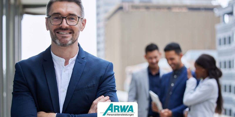 Lächelnder Vorgesetzter in Business-Anzug, der vor einem Team steht – ARWA Personaldienstleistungen.