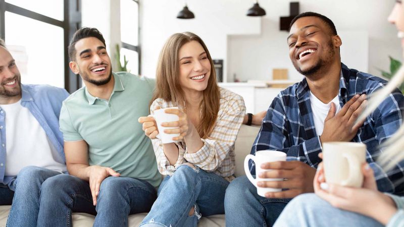 Gruppe von Freunden, die in einer entspannten Umgebung zusammen lachen und Kaffee trinken, was fÃ¼r positive soziale Interaktionen steht.