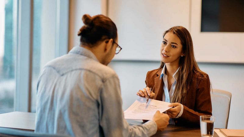 Personalerin und Bewerber im VorstellungsgesprÃ¤ch, sie erklÃ¤rt ein Dokument und stellt Fragen in einem modernen BÃ¼ro.