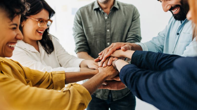 Lachendes Team legt die HÃ¤nde zusammen und zeigt Zusammenarbeit, die intrinsische Motivation fÃ¶rdert.