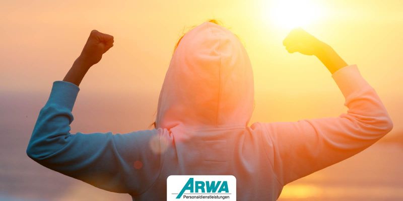 Person in Hoodie, die beide Arme triumphierend in die Luft streckt, mit Sonnenaufgang im Hintergrund – Arwa Personaldienstleistungen Logo darunter.