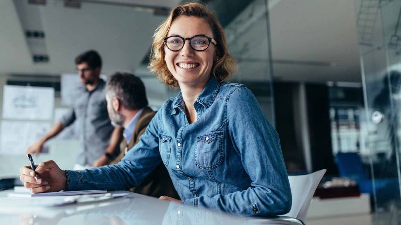 Eine Frau lÃ¤chelt wÃ¤hrend eines Meetings, wÃ¤hrend sie mit anderen Teilnehmern durch ihre paraverbale Kommunikation interagiert.