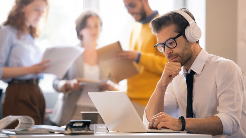 Konzentrierter Mann mit KopfhÃ¶rern arbeitet an einem Laptop in einem BÃ¼ro. Er symbolisiert die Faktoren, die die extrinsische Motivation beeinflussen, indem er sich auf seine Arbeit fokussiert.