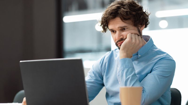 Nachdenklicher Mann vor einem Laptop, der auf ambivalentes Verhalten bei der Arbeit hinweist.