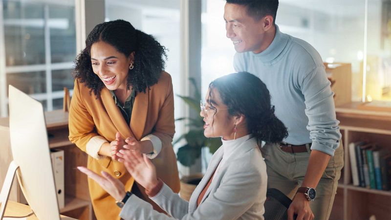 Drei motivierte Teammitglieder arbeiten gemeinsam an einem Projekt und lachen, symbolisch fÃ¼r den kooperativen FÃ¼hrungsstil mit Fokus auf Zusammenarbeit und Mitbestimmung.