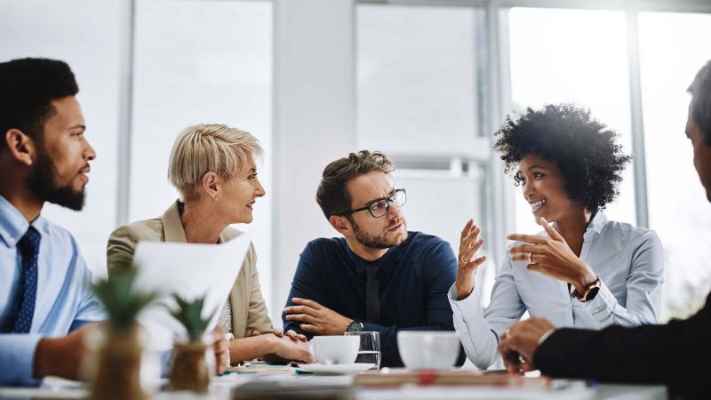 Ein Team in einem Meeting, das lebhaft diskutiert, mit einer FÃ¼hrungskraft, die aktiv zuhÃ¶rt und die Beteiligung fÃ¶rdert.