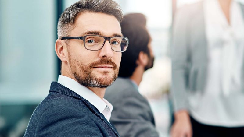 Selbstbewusster Mann mit Brille in einem Teammeeting â€“ symbolisiert den kooperativen FÃ¼hrungsstil, geprÃ¤gt von Mitbestimmung und Zusammenarbeit.